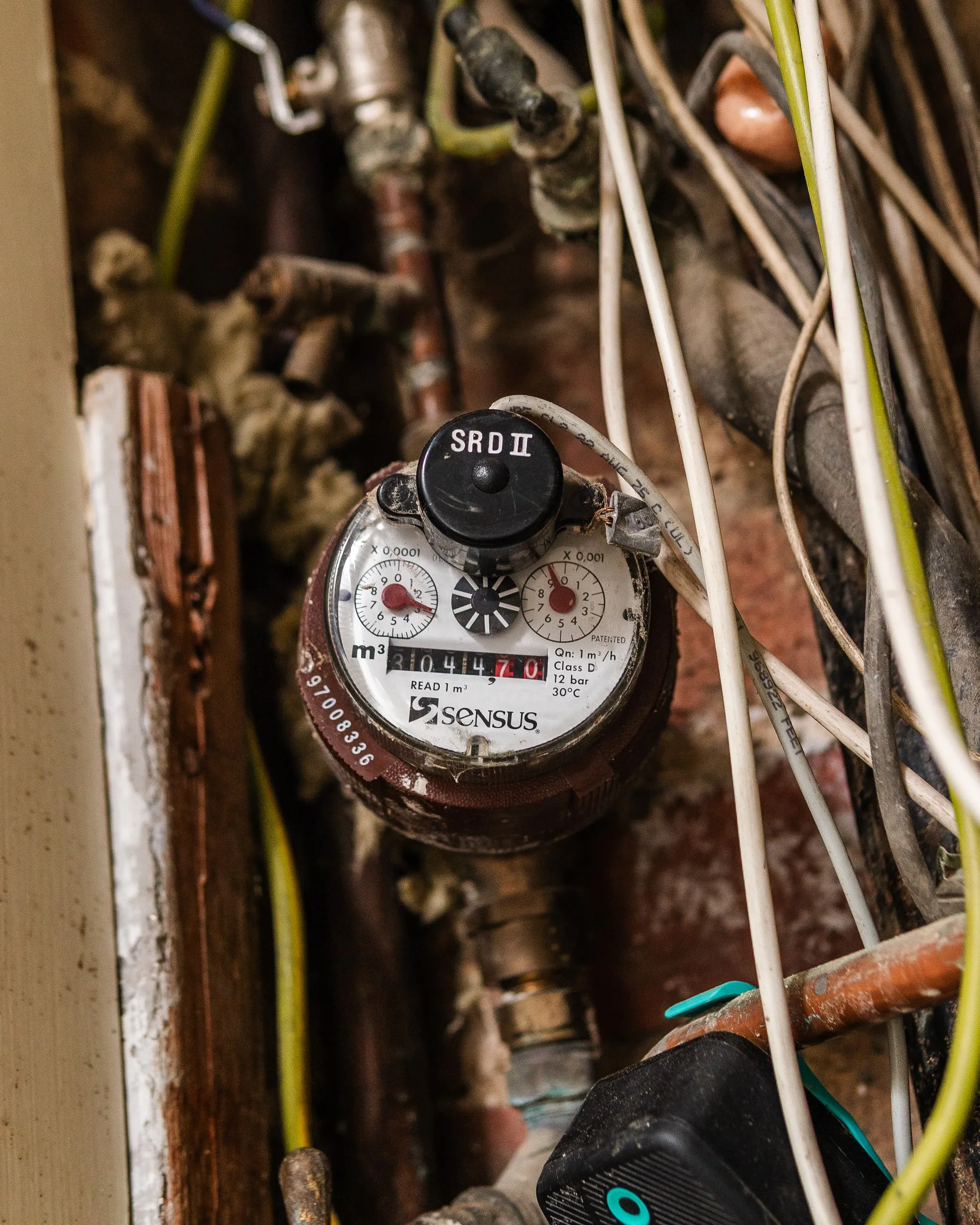 Close-up of a water meter dial among pipes and cables