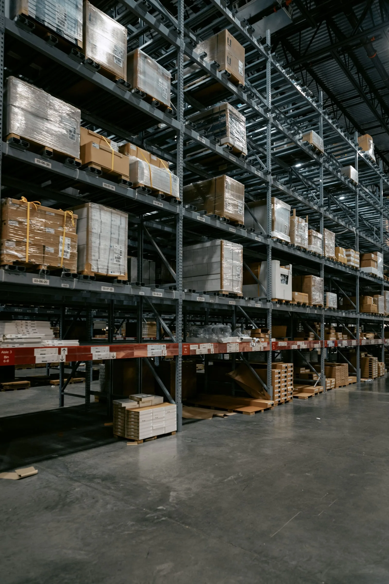 Tall pallet racking loaded with wrapped pallets and boxes above an empty concrete warehouse floor